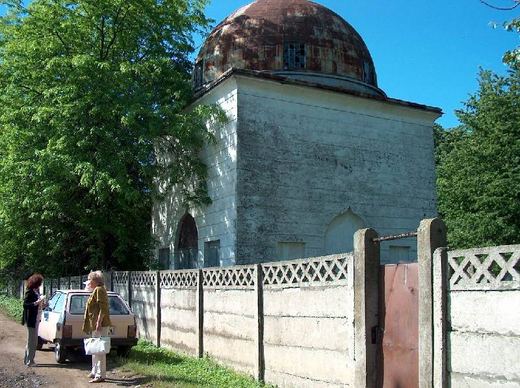 A domed ohel behind the cemetery wall, with visitors