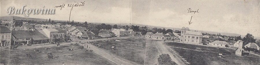 Wide panorama of an open square with roads and low houses; a handwritten arrow points to the twin-towered temple