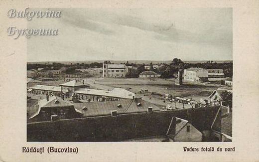 View over rooftops to a wide open square with carts and scattered buildings, a flat horizon beyond