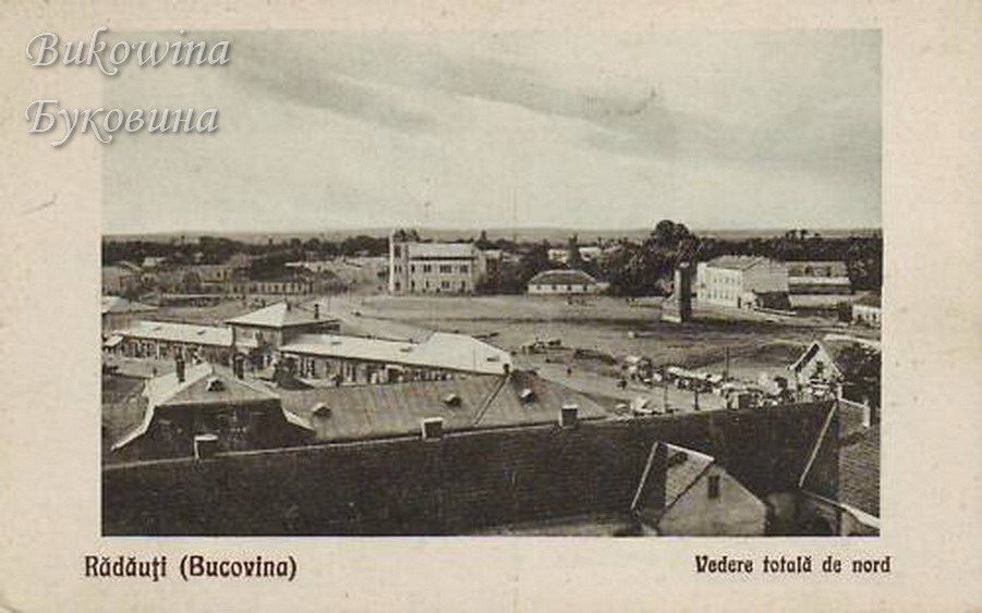 View over rooftops to a wide open square with carts and scattered buildings, a flat horizon beyond