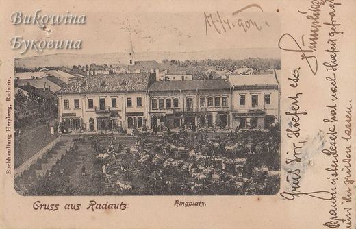 Market day on the square, packed with horse carts in front of a row of two-storey buildings; handwritten note