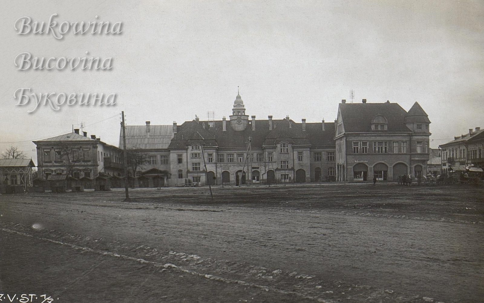 Broad empty square before the town hall with its domed clock tower, flanked by shops and wooden booths
