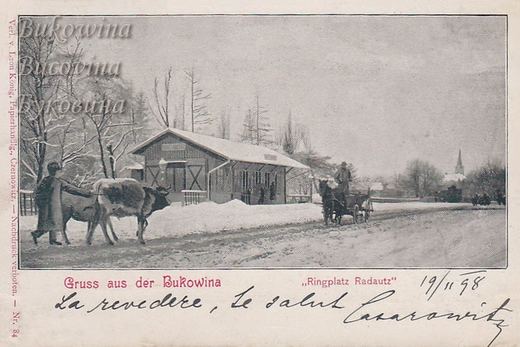 Snowy square with a timber pavilion, a man leading a cow, a horse cart and a church spire in the distance