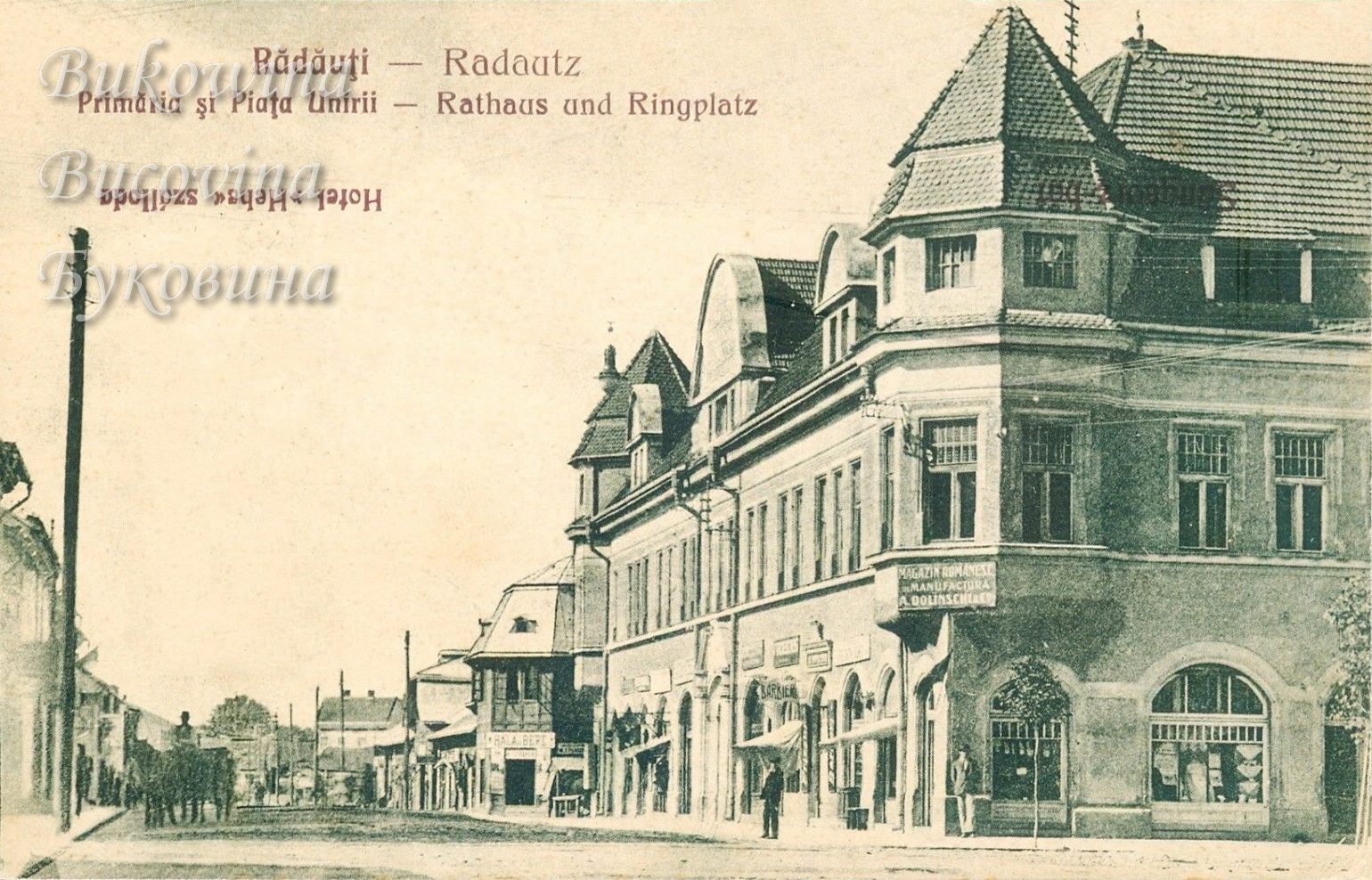 Large corner building with a steep-roofed tower and ground-floor shops, a long street stretching away on the left