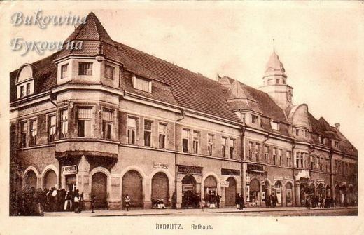 Sepia view of the long town hall with a domed clock tower, arched shopfronts and small groups of people