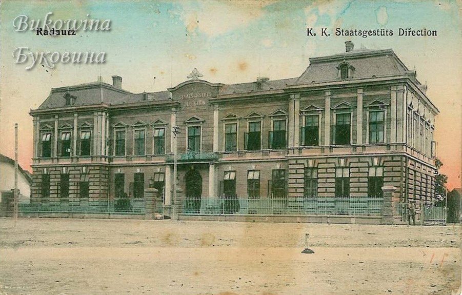 Coloured view of a grand building with a mansard roof and iron railings, facing an empty unpaved square