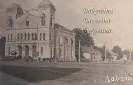 Large twin-domed synagogue with arched windows and entrances, horse carts in front and low houses beside it