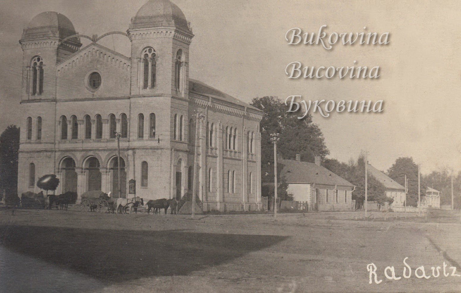 Large twin-domed synagogue with arched windows and entrances, horse carts in front and low houses beside it