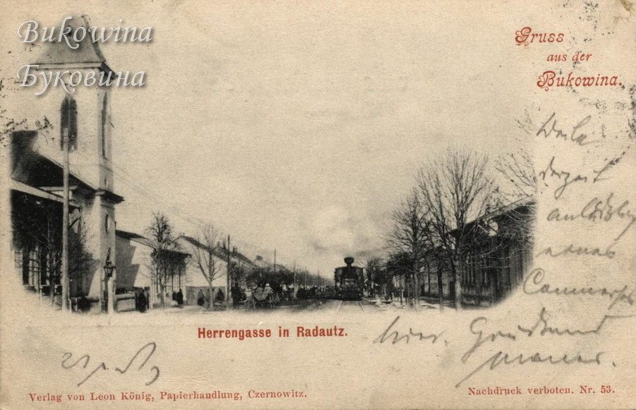 Steam locomotive running down a tree-lined street, a church tower and houses at left, handwritten note at right
