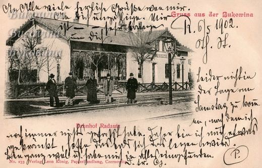 Five men in coats and hats on the tracks before a station building with a lamp post, handwriting across card