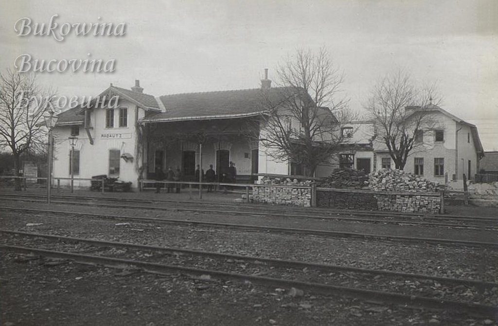 Station building signed Radautz across several tracks, men on the platform and piles of bricks beside it