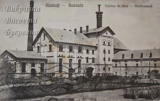 Large brewery complex with a tall chimney and a tower, rows of wooden barrels in the yard, postmarks across the front