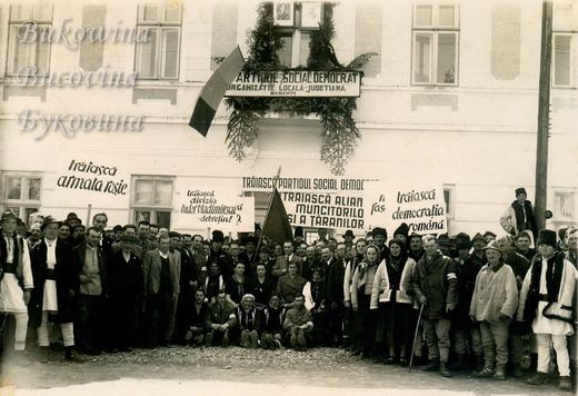 Crowd in coats and folk dress with banners and flags outside the Social Democratic Party office in Rădăuţi