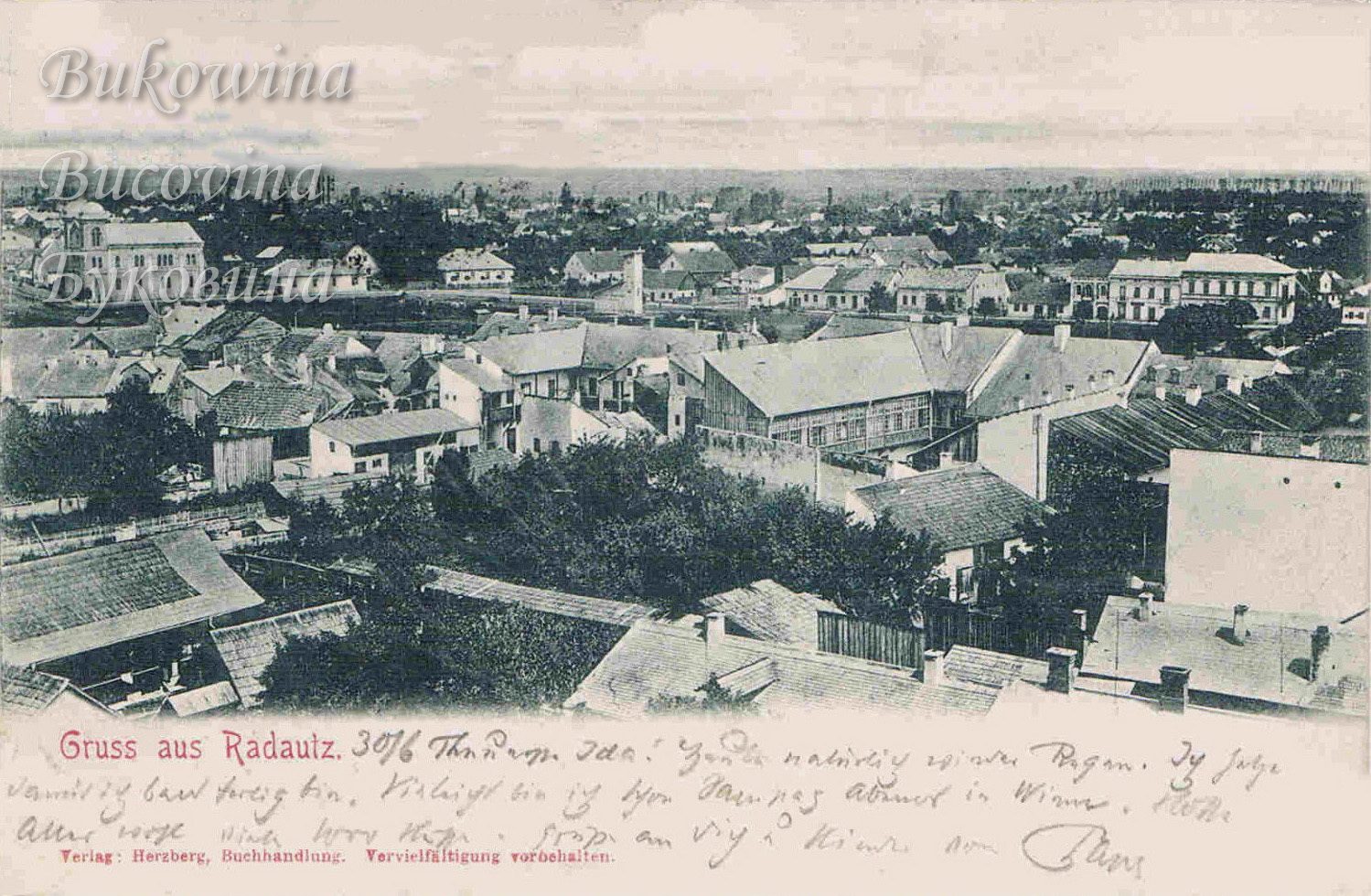 View over tiled rooftops and gardens to the flat town beyond, with a large twin-towered building at left; handwritten note