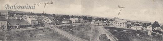 Wide panorama of an open square with roads and low houses; a handwritten arrow points to the twin-towered temple