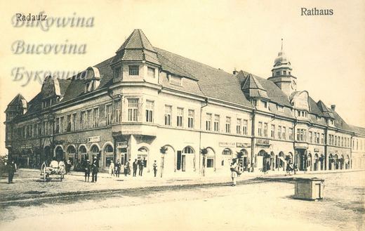 Long town hall with a corner tower and a domed clock tower, arched shopfronts, a cart and people on the square