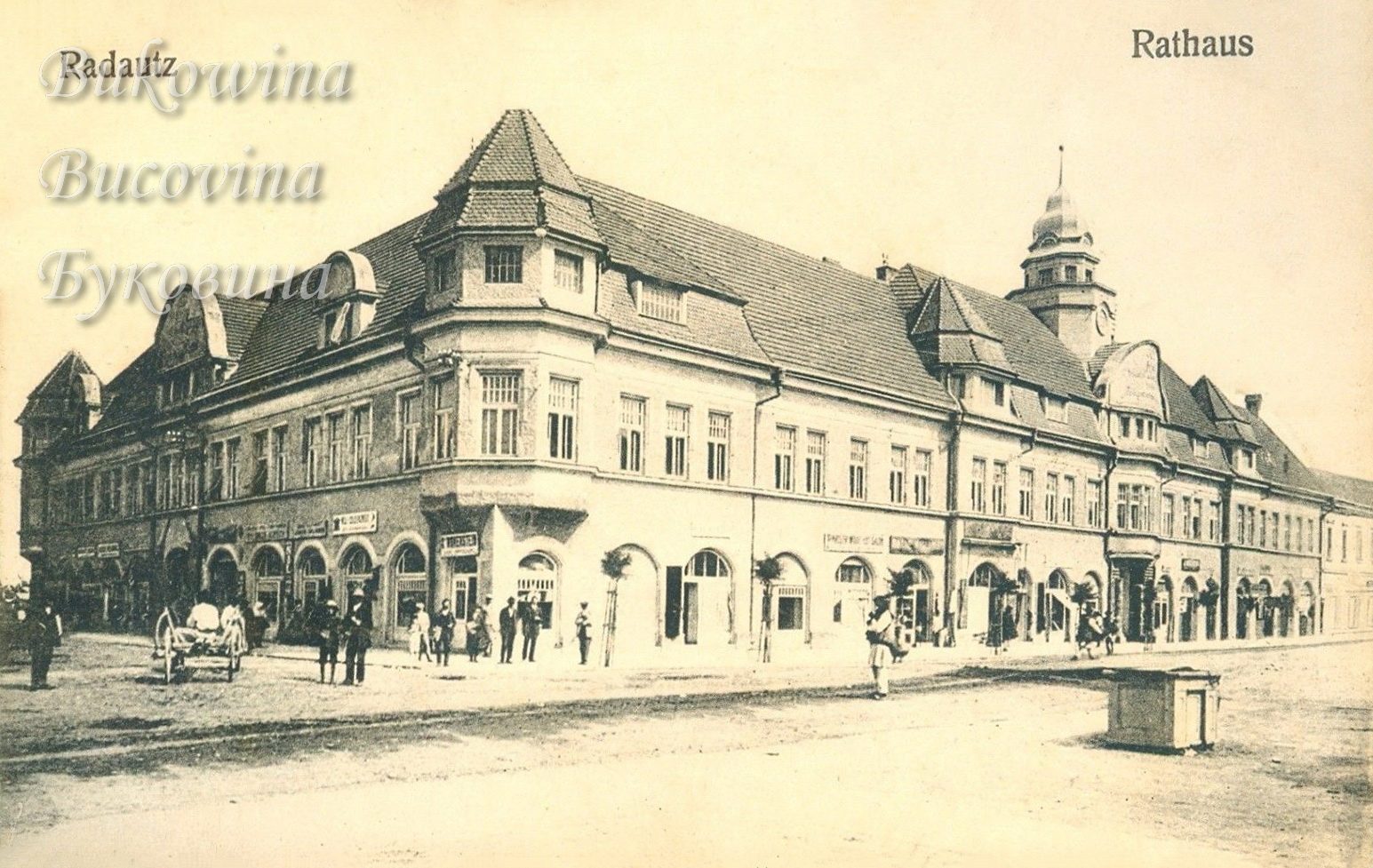 Long town hall with a corner tower and a domed clock tower, arched shopfronts, a cart and people on the square