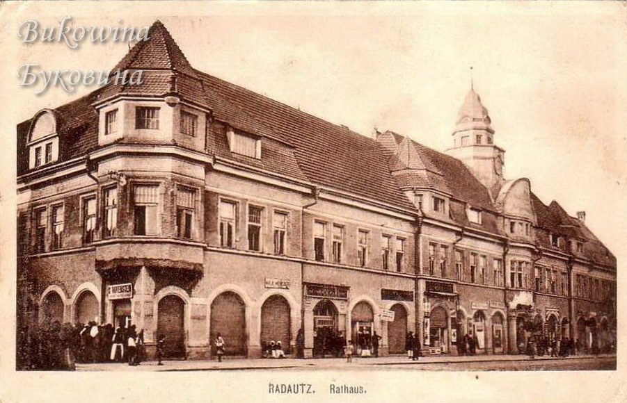 Sepia view of the long town hall with a domed clock tower, arched shopfronts and small groups of people