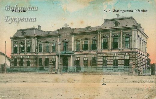Coloured view of a grand building with a mansard roof and iron railings, facing an empty unpaved square