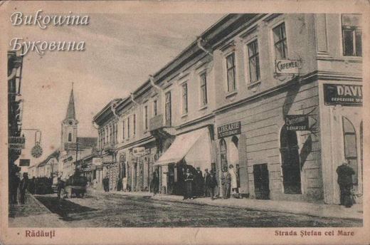 Street of two-storey buildings with a bookshop sign and an awning, people on the pavement and a church spire
