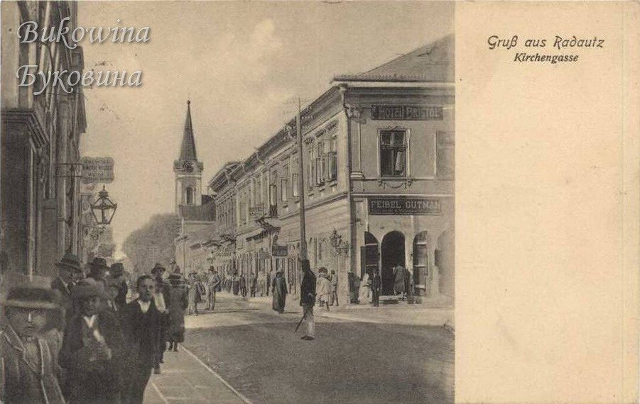 Street with Hotel Bristol and the shop sign Feibel Gutman on a corner building, pedestrians and a church spire