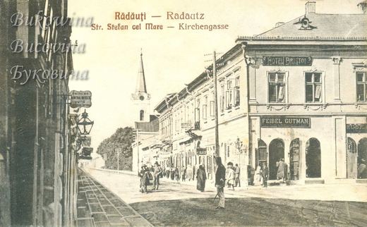 Street with Hotel Bristol and Feibel Gutman signs, a church spire and a mineral water sign with Hebrew letters