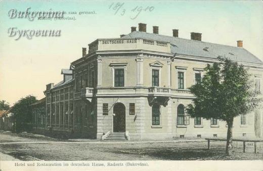 Coloured view of a two-storey corner building with Deutsches Haus on the parapet and a tree in front