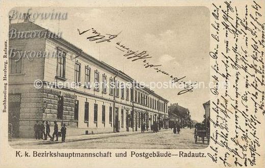 Long two-storey government building along a street, men standing at the corner, handwritten message at right