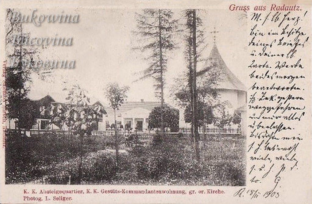Garden with tall trees before low buildings and a church with a high conical roof, handwritten note at right