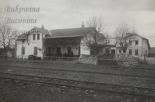 Station building signed Radautz across several tracks, men on the platform and piles of bricks beside it