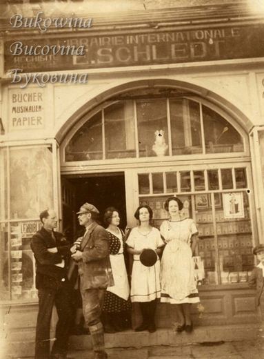 Two men and three women posing at the arched doorway of a bookshop signed Librairie Internationale E. Schledt