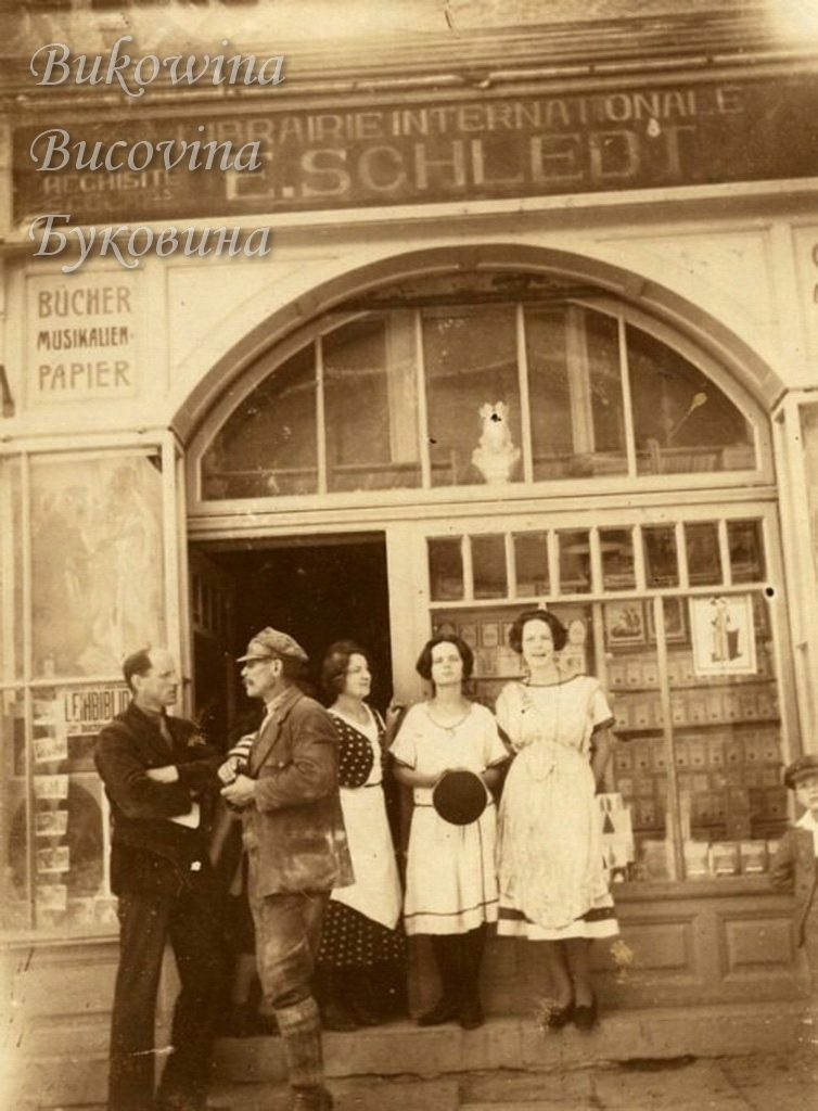 Two men and three women posing at the arched doorway of a bookshop signed Librairie Internationale E. Schledt