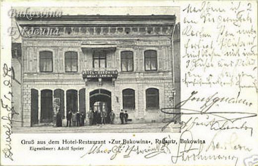 Two-storey hotel facade with arched ground-floor openings, men standing at the entrance, handwriting around it