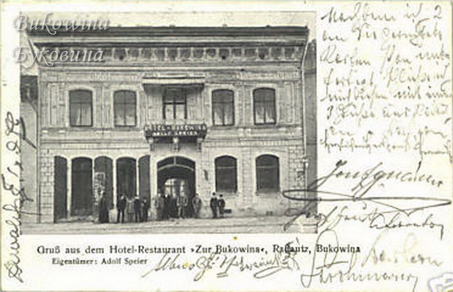 Two-storey hotel facade with arched ground-floor openings, men standing at the entrance, handwriting around it