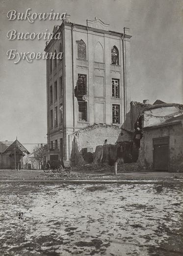 Tall building with pointed-arch windows, shattered panes and a collapsed side wall, a horse cart and rubble in front