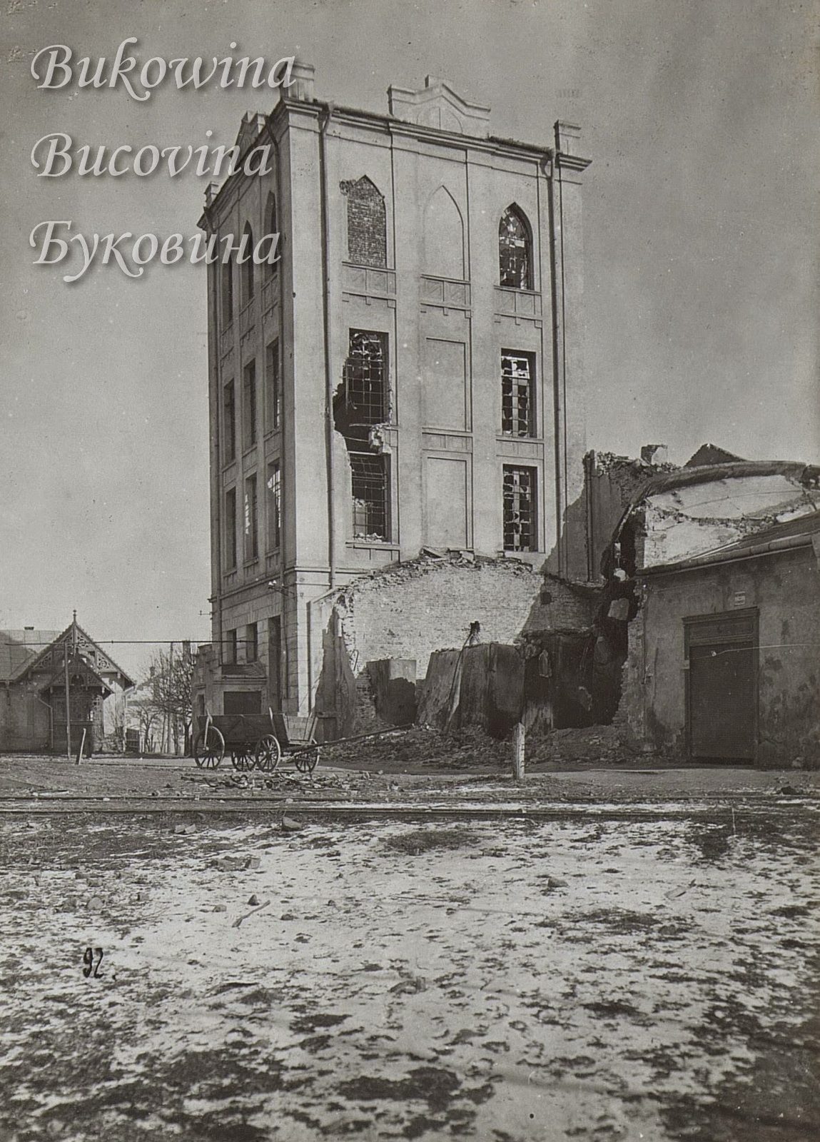 Tall building with pointed-arch windows, shattered panes and a collapsed side wall, a horse cart and rubble in front