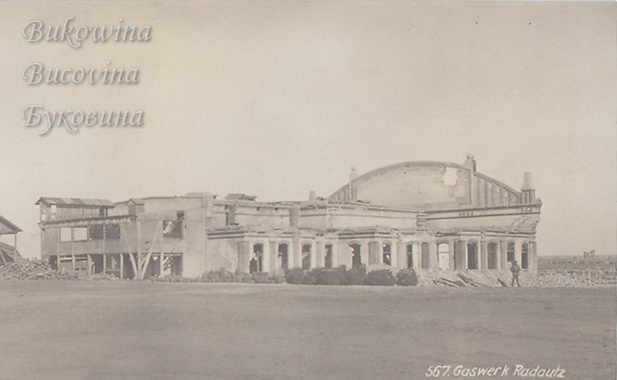 Ruined gasworks building with an arched roofline, broken walls and rubble, a lone soldier standing in front