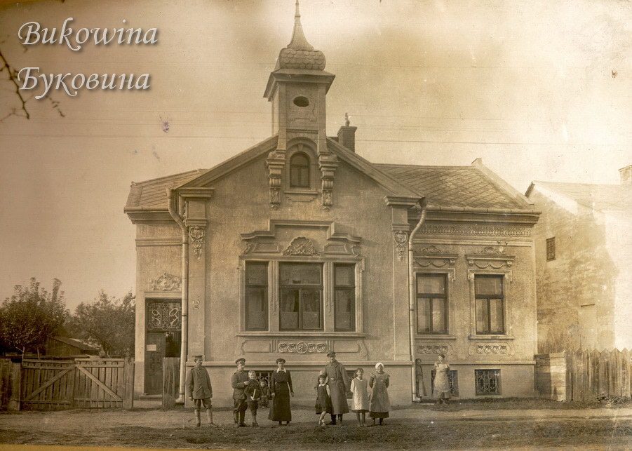 Single-storey house with stucco ornament and a small domed turret, a family and soldiers standing in front